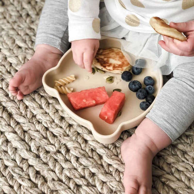 Baby enjoying food on a bear-shaped silicone plate with watermelon, blueberries, pancakes, and pasta. Safe for infants 3 months and up.